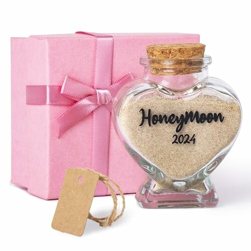 Heart-shaped glass bottle with 'Honeymoon 2024' sand, next to a pink gift box.