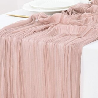 Pink gauze table runner draped over a white table with plates and utensils.