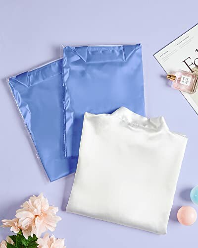 Folded silk shirts with perfume and flowers on a table.