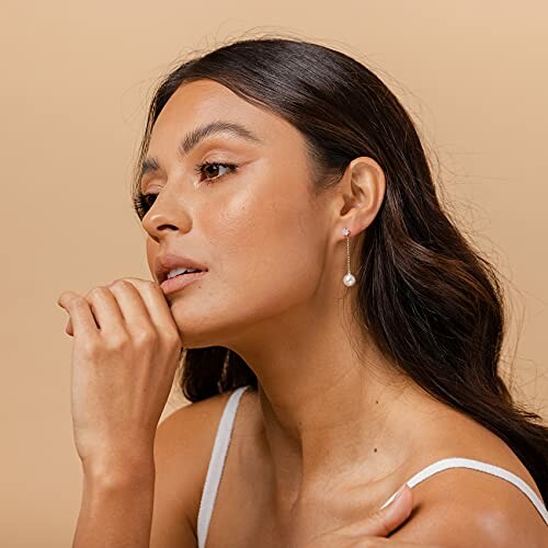 Woman with long hair wearing pearl drop earrings.